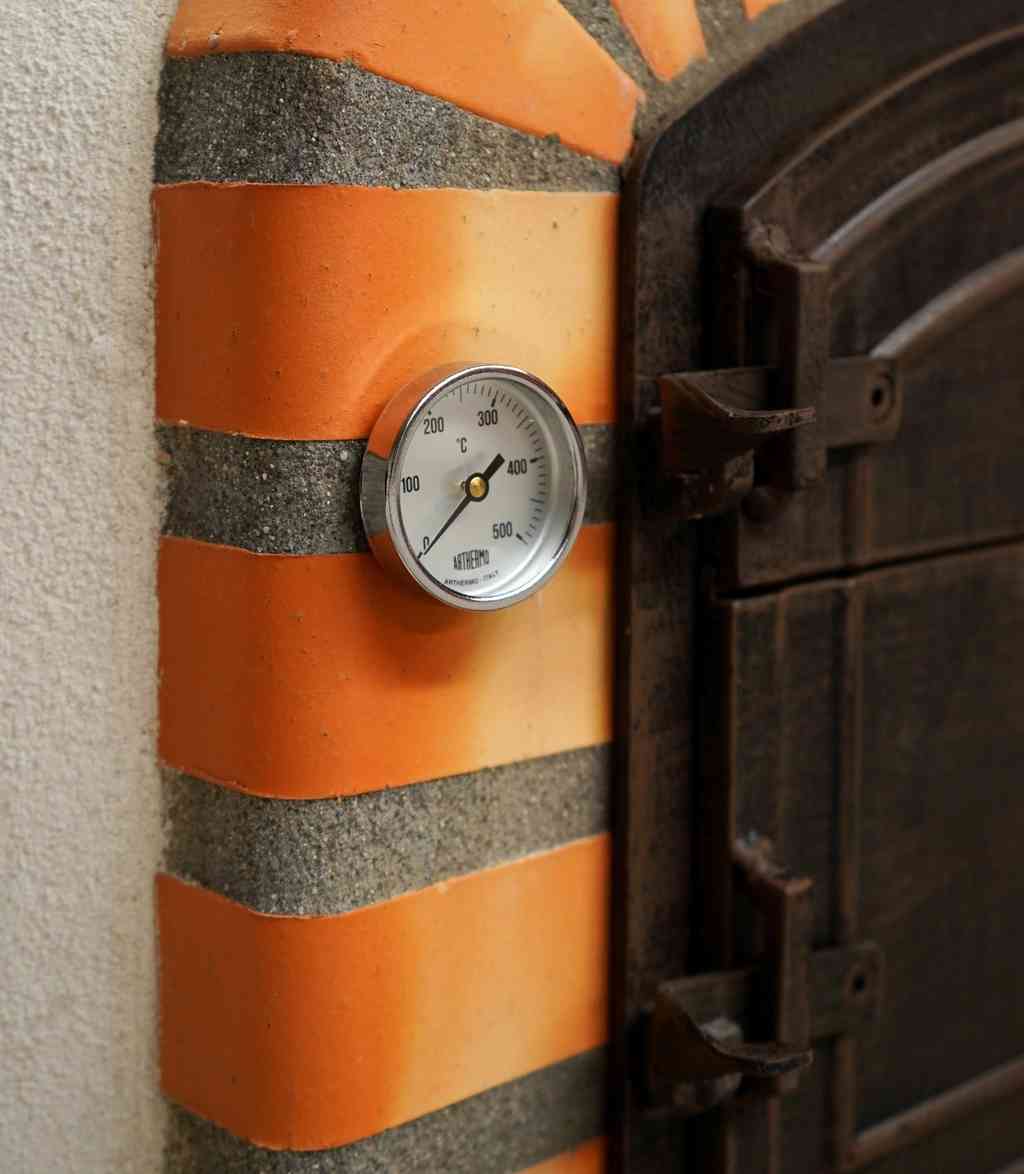 Close-up van een ingebouwde analoge thermometer in de oranje-rode terracotta boog van een steenoven