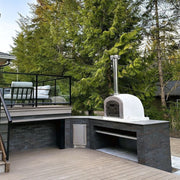 Witte houtgestookte steenoven op een moderne strakke buitenkeuken van donkere steen op een houten terras