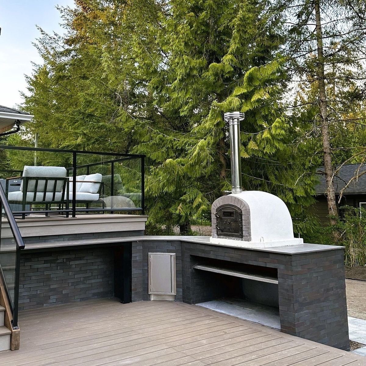 Witte houtgestookte steenoven op een moderne strakke buitenkeuken van donkere steen op een houten terras